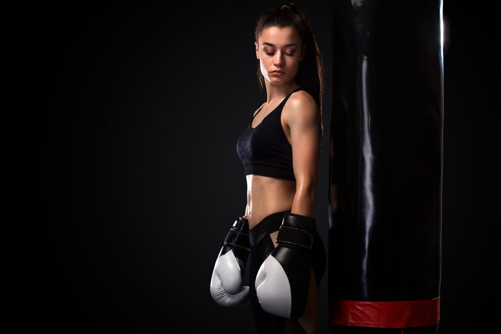 Woman boxer fighting in gloves with boxing punching bag on black background. Boxing and fitness concept.
